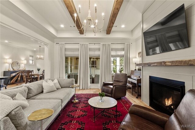 living area featuring light wood finished floors, beamed ceiling, recessed lighting, an inviting chandelier, and a glass covered fireplace