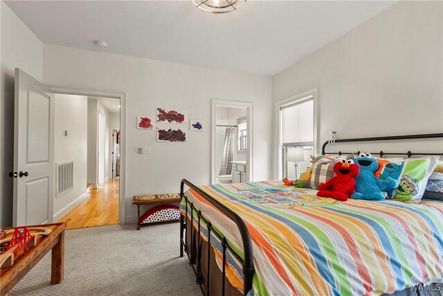 bedroom featuring visible vents, light colored carpet, and ensuite bath