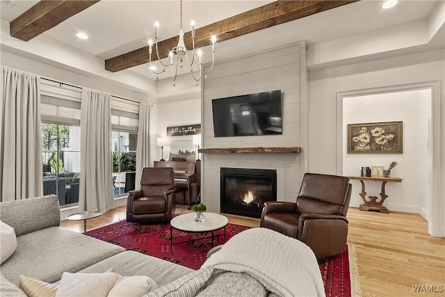 living room with wood finished floors, baseboards, beam ceiling, a large fireplace, and a chandelier