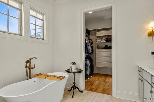 full bath with a spacious closet, baseboards, a freestanding bath, wood finished floors, and vanity