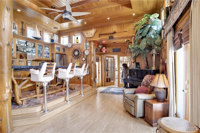 home office with light wood-type flooring, wooden ceiling, wooden walls, and a bar