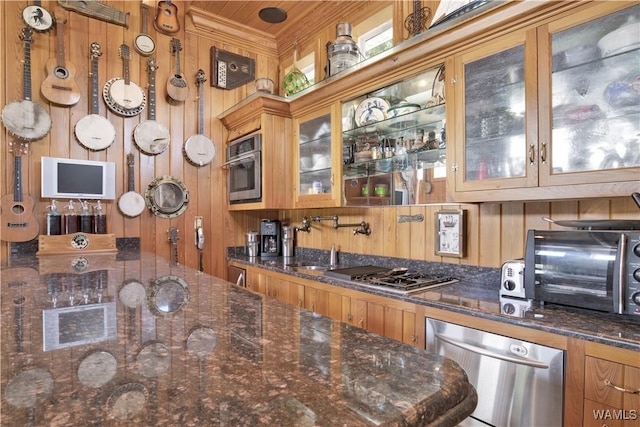 kitchen with appliances with stainless steel finishes, brown cabinets, glass insert cabinets, and wooden walls