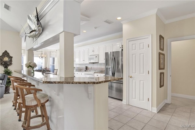 kitchen featuring white appliances, visible vents, decorative backsplash, a kitchen breakfast bar, and dark stone countertops