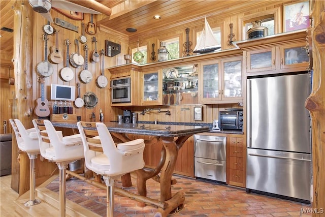 kitchen with wood ceiling, glass insert cabinets, appliances with stainless steel finishes, brick floor, and wood walls