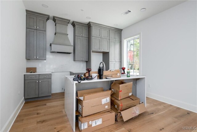 1300 Paul W Bryant Dr Unit 100, Tuscaloosa, AL 35401 - kitchen with gray cabinetry, custom range hood, light wood-style flooring, and a kitchen island with sink