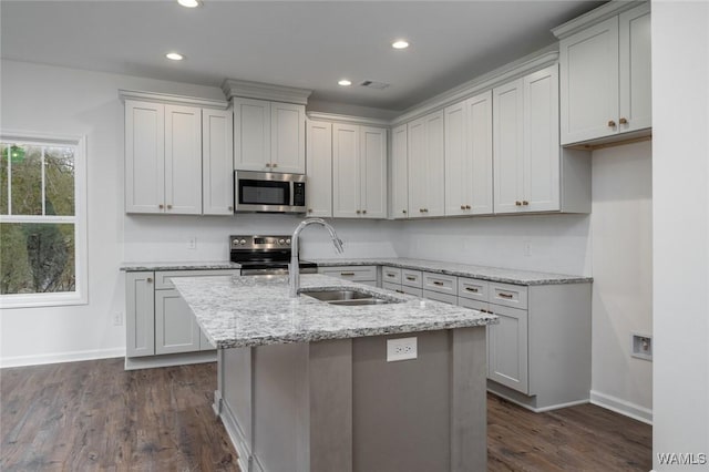 kitchen featuring light stone countertops, stainless steel appliances, a kitchen island with sink, and dark wood-type flooring