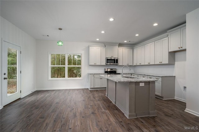 kitchen with appliances with stainless steel finishes, light stone counters, a kitchen island with sink, dark wood-type flooring, and sink