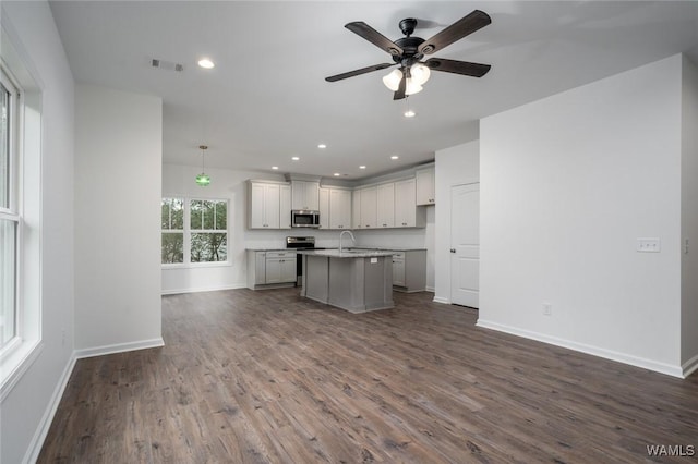 kitchen with a center island with sink, hanging light fixtures, ceiling fan, dark hardwood / wood-style flooring, and stainless steel appliances