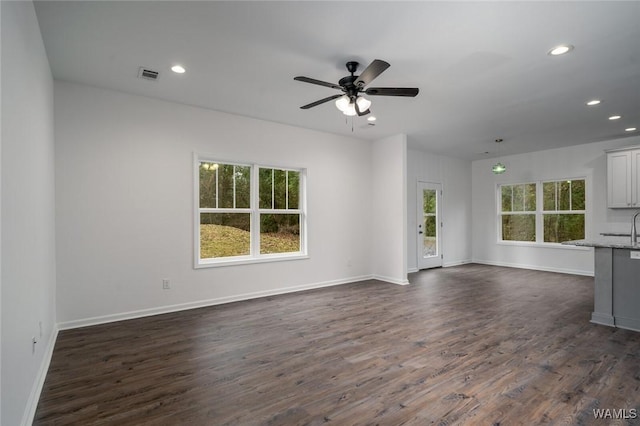 unfurnished living room featuring ceiling fan, dark wood-type flooring, and a wealth of natural light