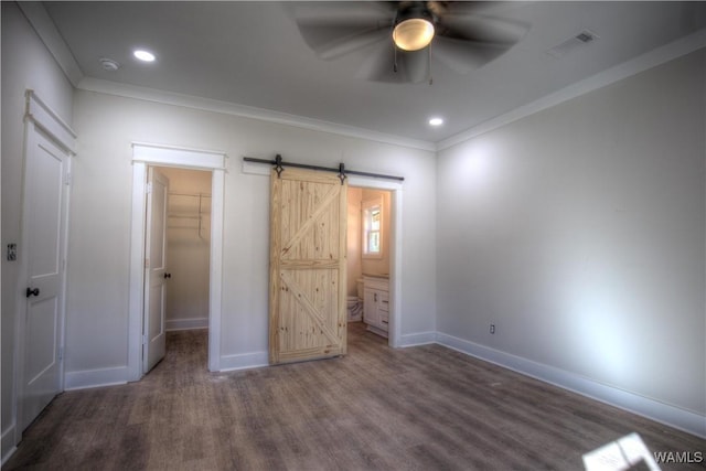 unfurnished bedroom with a walk in closet, visible vents, a barn door, ornamental molding, and wood finished floors