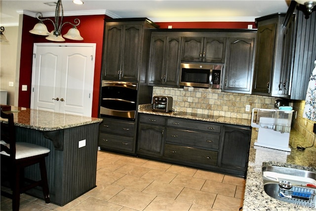 kitchen with hanging light fixtures, stainless steel appliances, light stone counters, a notable chandelier, and backsplash