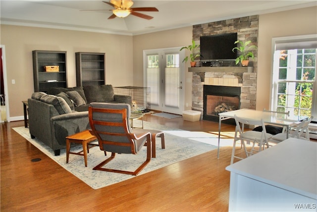 living room with hardwood / wood-style floors, crown molding, a healthy amount of sunlight, and a stone fireplace