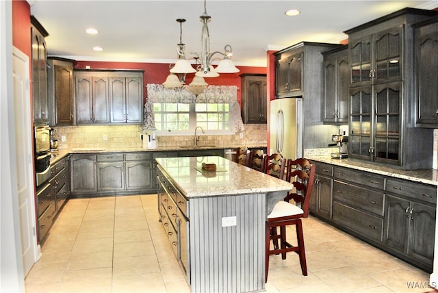 kitchen with sink, pendant lighting, light tile patterned floors, a kitchen island, and stainless steel refrigerator