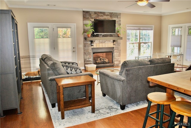 living room featuring dark hardwood / wood-style flooring, a stone fireplace, ceiling fan, and crown molding