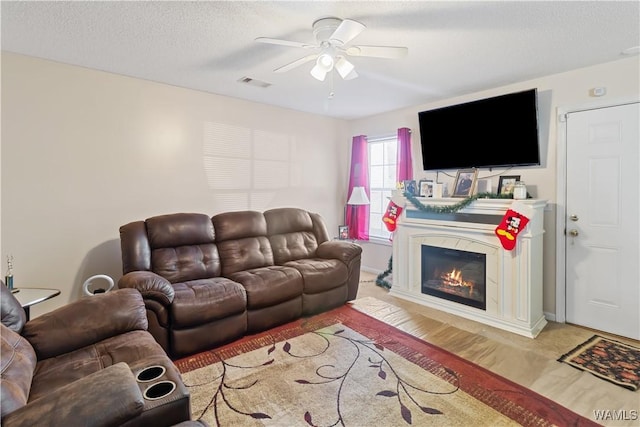 living room with ceiling fan, a textured ceiling, and light wood-type flooring