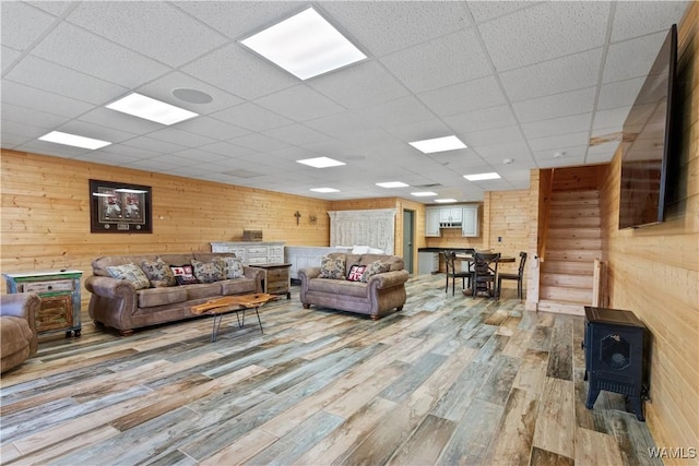 living room with wooden walls, wood finished floors, a wood stove, and a paneled ceiling