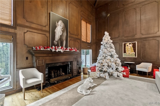 living area with a high end fireplace, light hardwood / wood-style floors, and wood walls