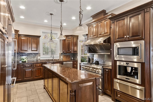 kitchen with appliances with stainless steel finishes, dark stone counters, pendant lighting, a kitchen island, and ornamental molding