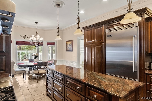 kitchen featuring stainless steel built in refrigerator, a notable chandelier, dark stone counters, pendant lighting, and ornamental molding