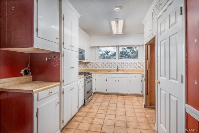 kitchen with sink, stainless steel appliances, light tile patterned floors, decorative backsplash, and white cabinets