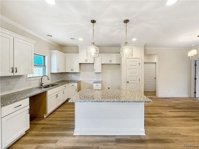 kitchen with a kitchen island, sink, pendant lighting, and white cabinets