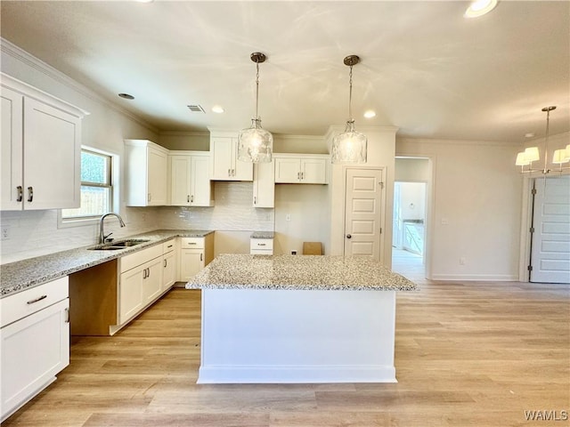 kitchen with pendant lighting, a kitchen island, sink, white cabinets, and light stone counters