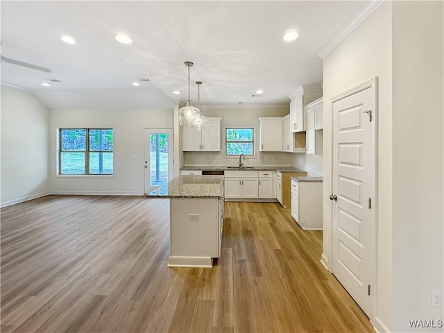 kitchen featuring sink, white cabinetry, a center island, light stone countertops, and decorative light fixtures