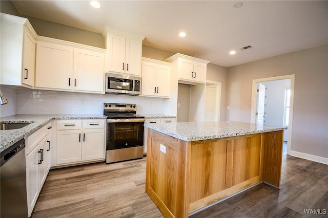 kitchen featuring appliances with stainless steel finishes, white cabinets, a center island, and hardwood / wood-style flooring