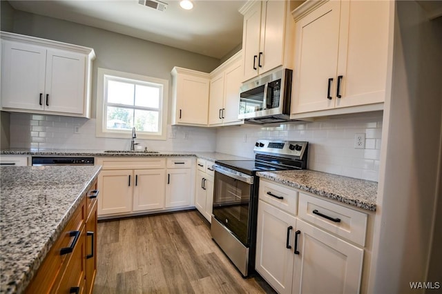 kitchen with sink, stainless steel appliances, white cabinetry, and light stone countertops