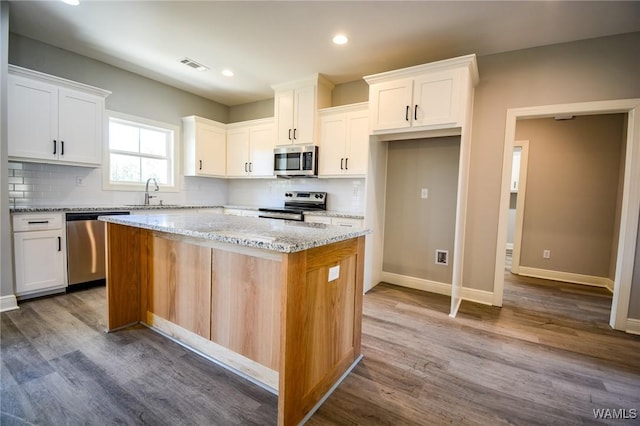 kitchen with a kitchen island, white cabinets, light stone counters, and appliances with stainless steel finishes