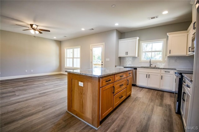 kitchen with light stone countertops, tasteful backsplash, a kitchen island, white cabinets, and appliances with stainless steel finishes