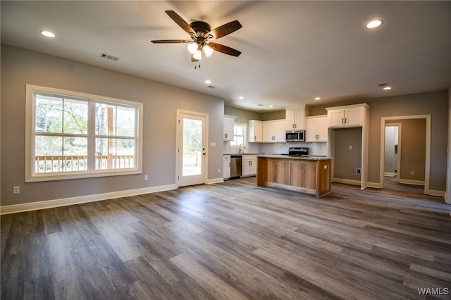 kitchen with appliances with stainless steel finishes, dark wood-type flooring, white cabinetry, and a kitchen island