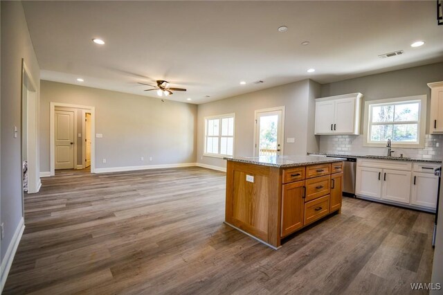 kitchen featuring dishwasher, light stone counters, a kitchen island, hardwood / wood-style flooring, and white cabinetry