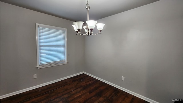 spare room with a notable chandelier and dark wood-type flooring