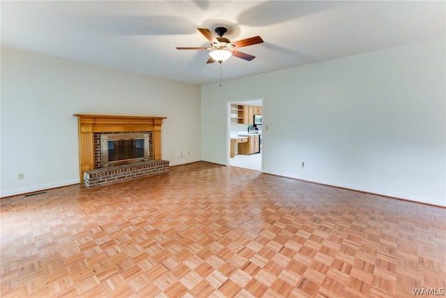 unfurnished living room featuring a textured ceiling, light parquet flooring, a brick fireplace, and ceiling fan