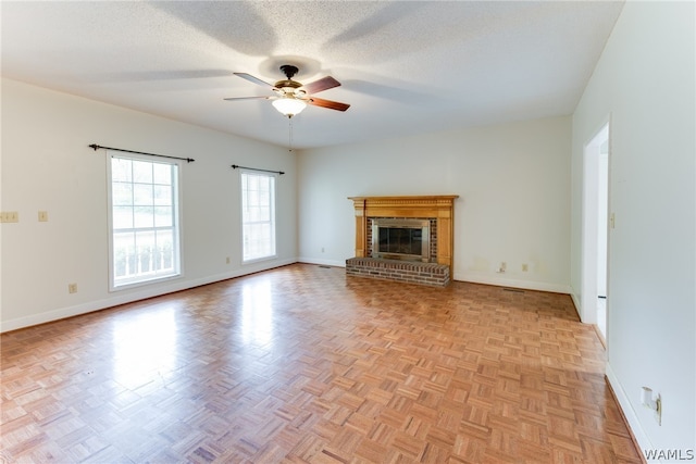 unfurnished living room featuring ceiling fan, a fireplace, light parquet floors, and a textured ceiling