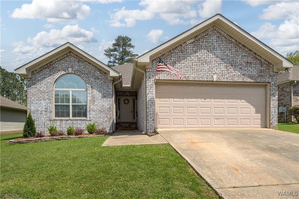 ranch-style home with a garage, brick siding, driveway, and a front lawn