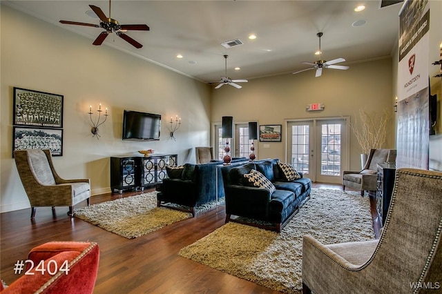 living area featuring french doors, visible vents, a towering ceiling, ornamental molding, and wood finished floors