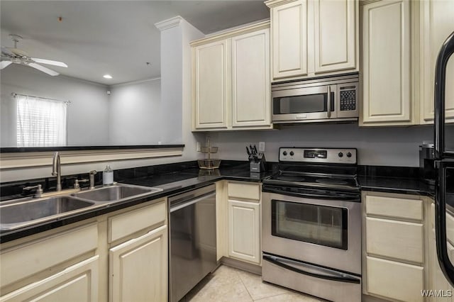 kitchen with light tile patterned floors, cream cabinets, a sink, appliances with stainless steel finishes, and dark countertops