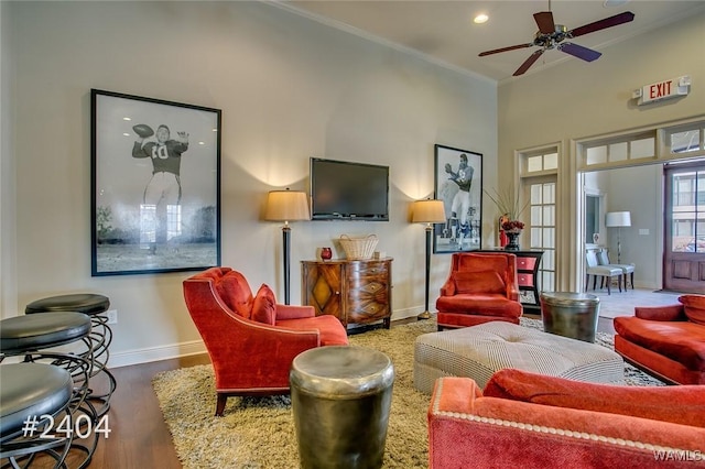 living area with ornamental molding, ceiling fan, baseboards, and wood finished floors