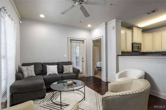 living area with ornamental molding, wood finished floors, visible vents, and baseboards