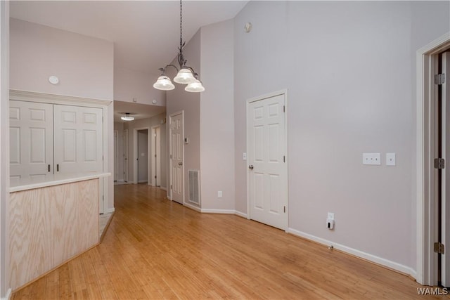 unfurnished dining area with a notable chandelier, light hardwood / wood-style flooring, and high vaulted ceiling