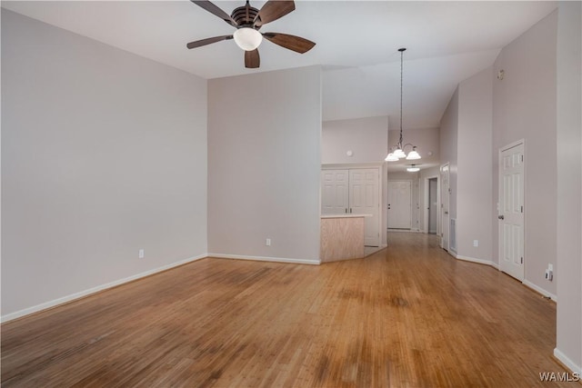 unfurnished living room with ceiling fan with notable chandelier, high vaulted ceiling, and light wood-type flooring