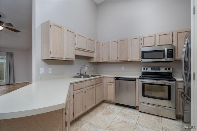 kitchen with appliances with stainless steel finishes, kitchen peninsula, sink, and light brown cabinets