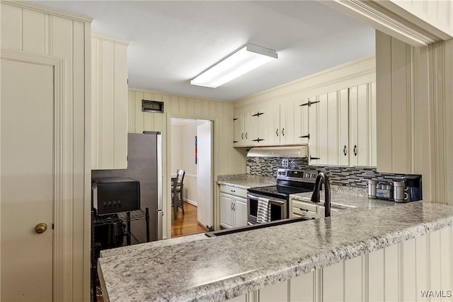 kitchen with a peninsula, tasteful backsplash, cream cabinetry, and electric stove