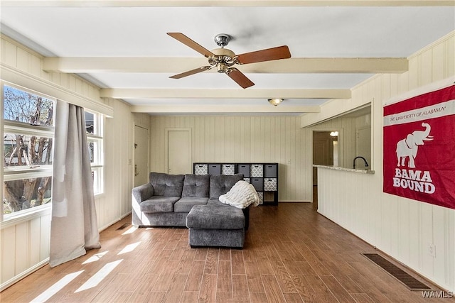 living area with ceiling fan, beam ceiling, and wood finished floors