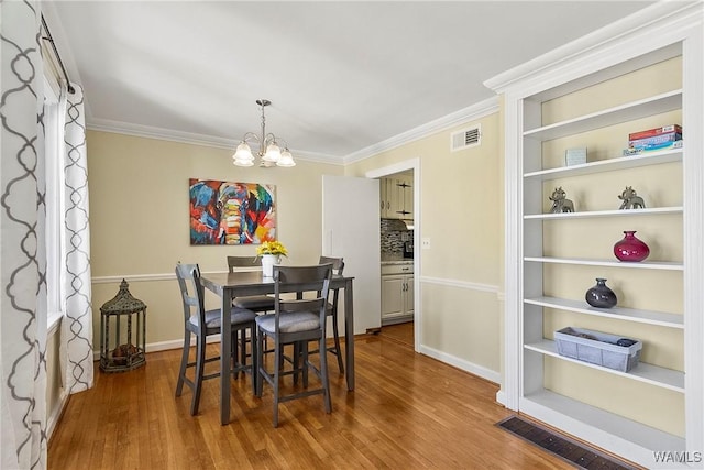 dining room featuring a chandelier, visible vents, crown molding, and wood finished floors