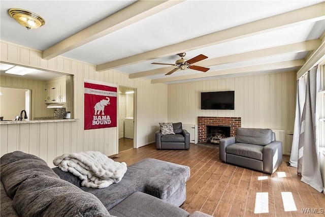 living room with a ceiling fan, beam ceiling, a fireplace, and wood finished floors