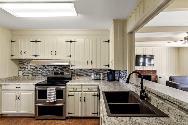 kitchen featuring decorative backsplash, a ceiling fan, range with two ovens, under cabinet range hood, and a sink