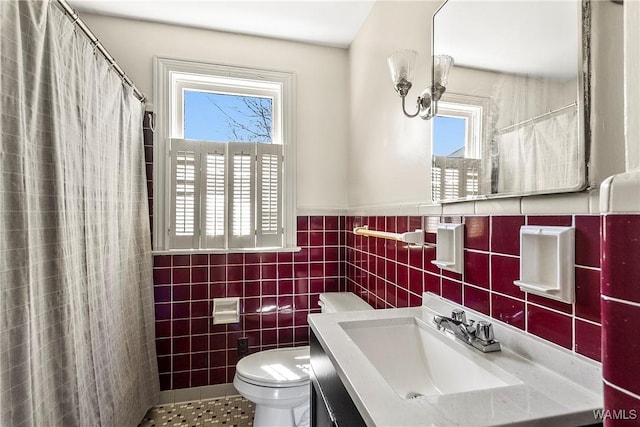 full bathroom featuring toilet, vanity, a wealth of natural light, and tile walls